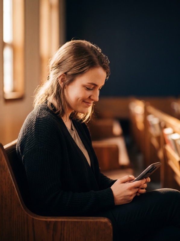 Woman in church pew smiling at her phone in warm amber light